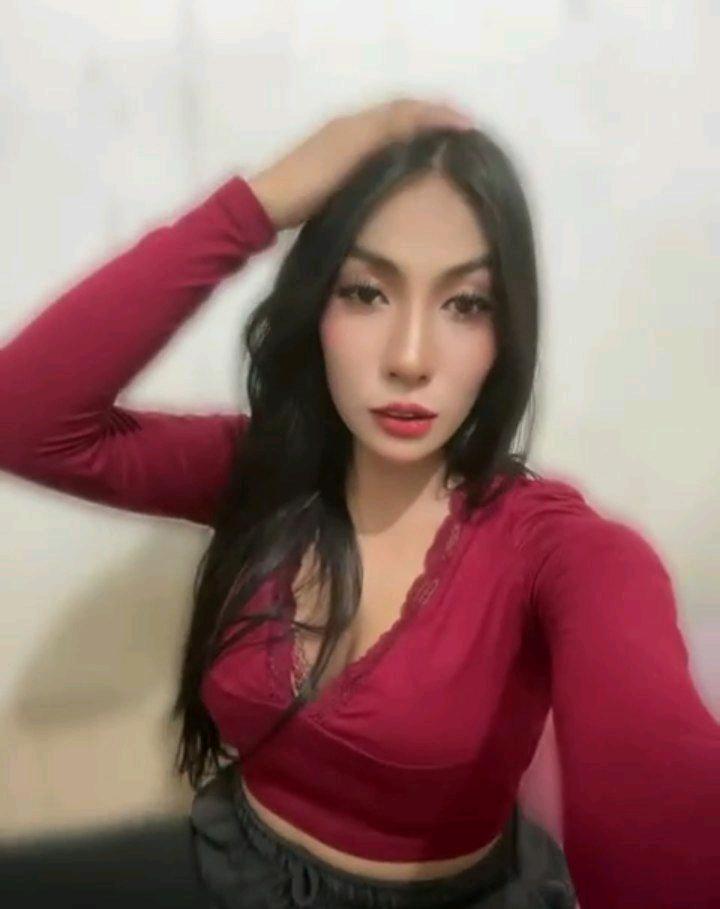 Woman with long dark hair in a red top, hand in her hair